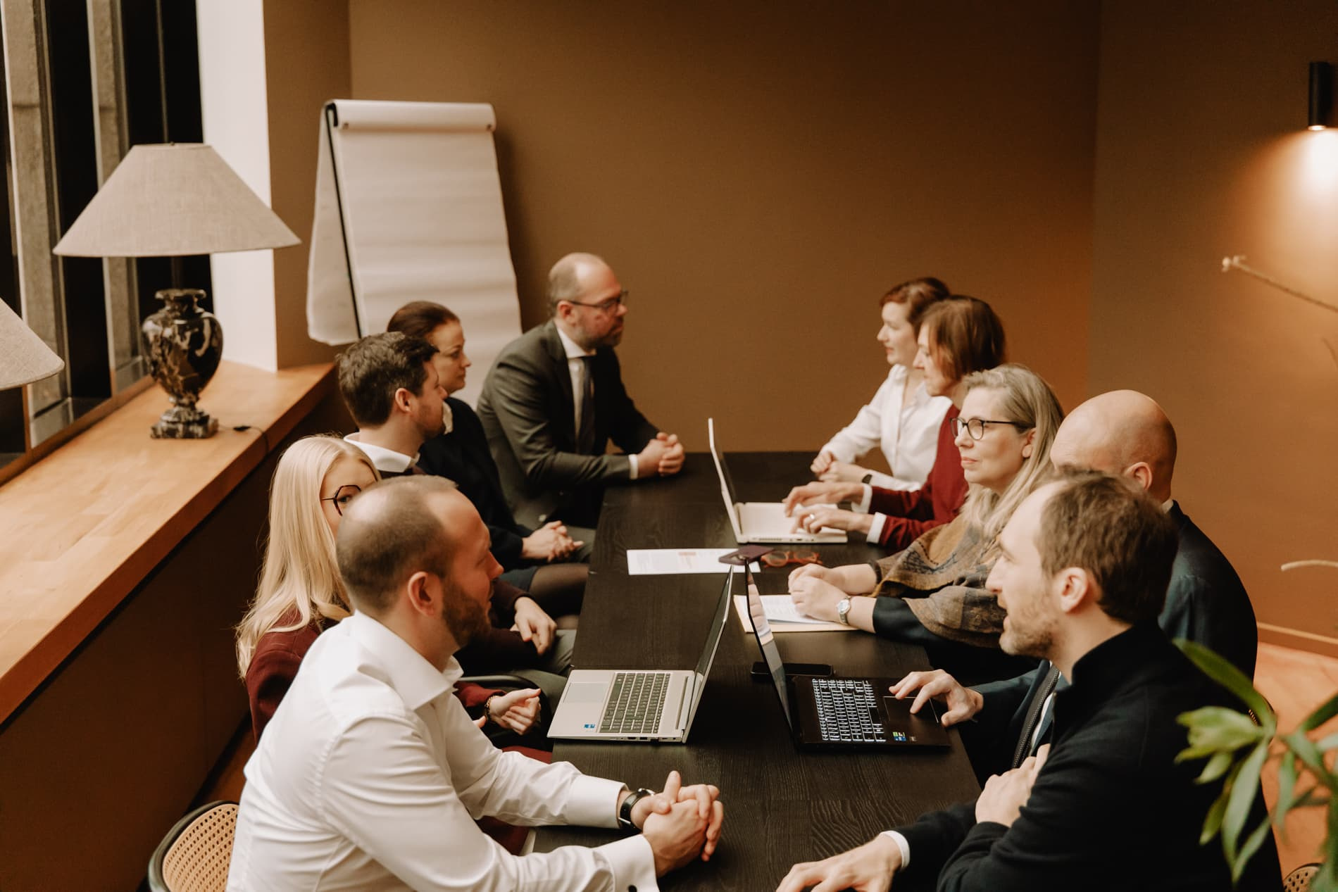 Een groep professionals zit rond een tafel in een kantoorruimte, bezig met een vergadering of bespreking.