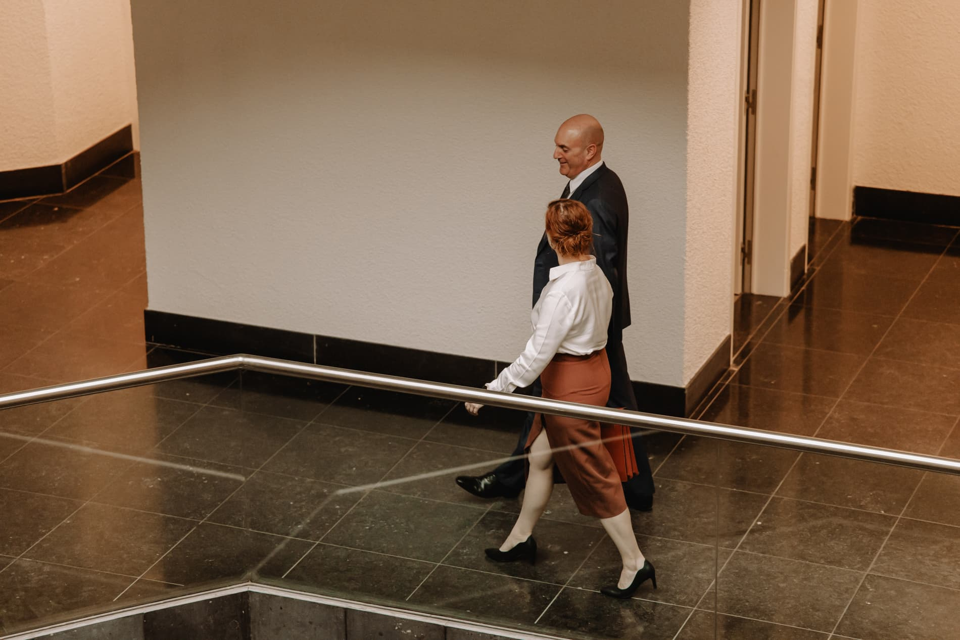 Een man en een vrouw in formele kleding lopen door een moderne, lichte kantoorruimte.