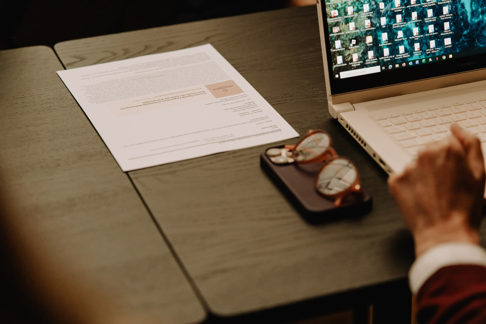 Een bureau met een laptop, een document en een paar brillen op een tray.