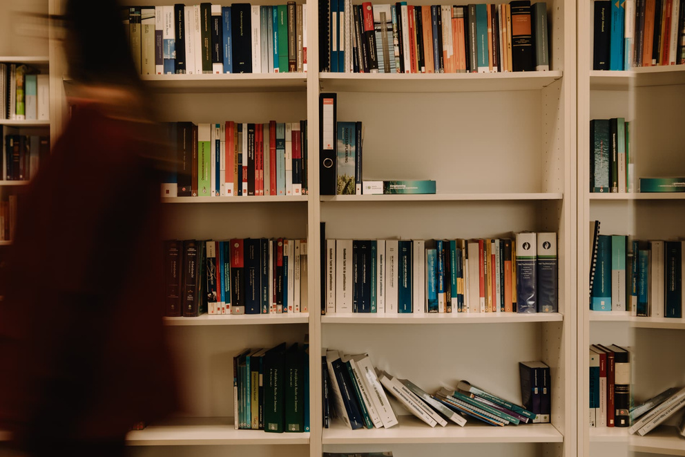 Twee boekenplanken gevuld met boeken, met een persoon in beweging op de voorgrond.